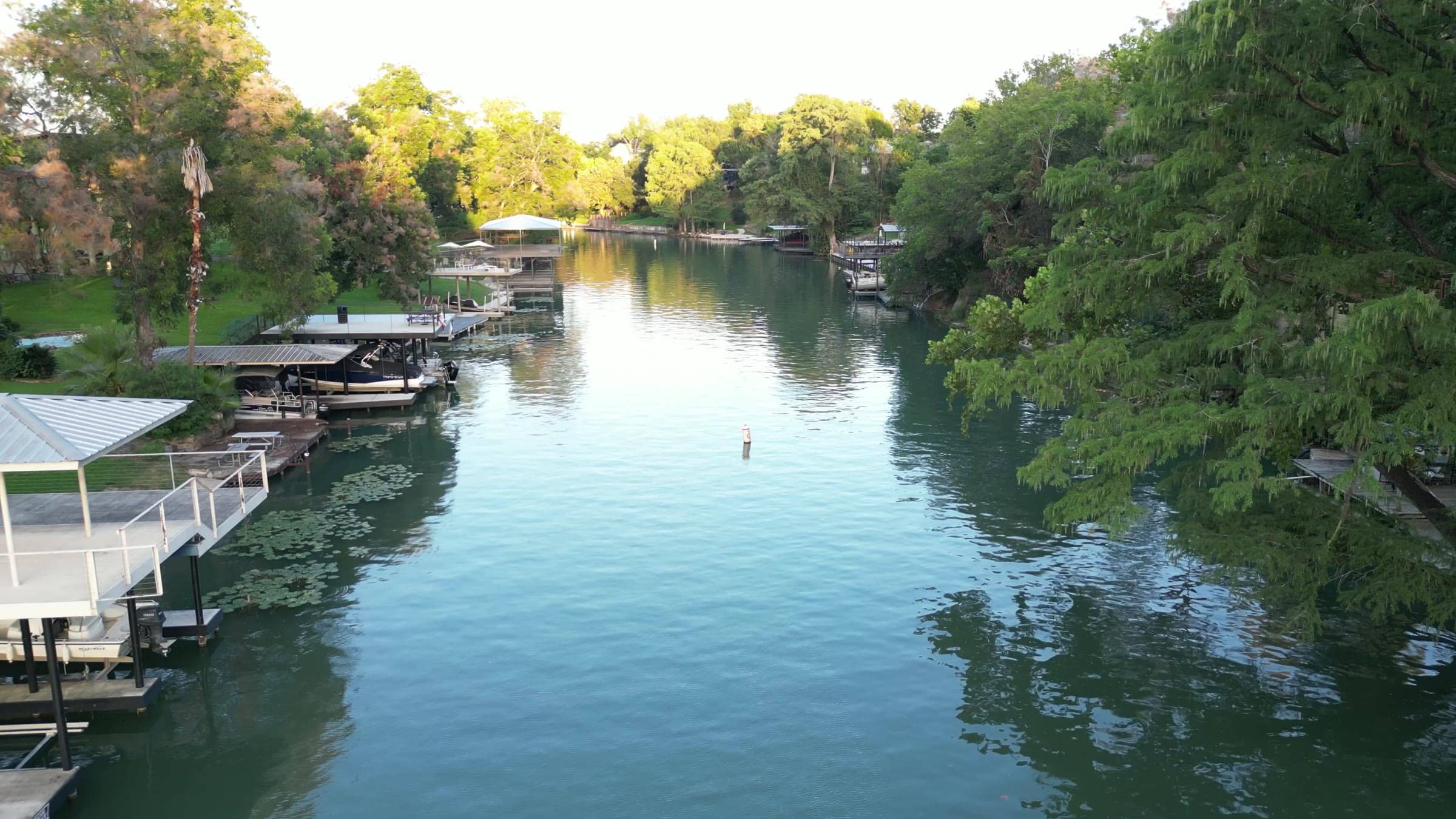 Aerial view looking down a tree-lined stretch of the Guadalupe River at Lake Dunlap, with boat docks along the bank